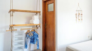 Una habitación con puerta de madera, un estante con toallas dobladas y un móvil de viento colgado en la pared.