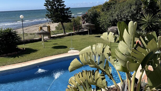 Ein Pool mit Blick auf den Ozean, umgeben von tropischen Pflanzen und einem gepflegten Rasen.