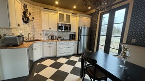 A kitchen with white cabinets, a black and white checkered floor, a dining table with chairs, a chandelier, and a view through a window.