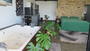 Una habitación moderna con una bañera grande, una cama con manta verde y una pared de piedra.