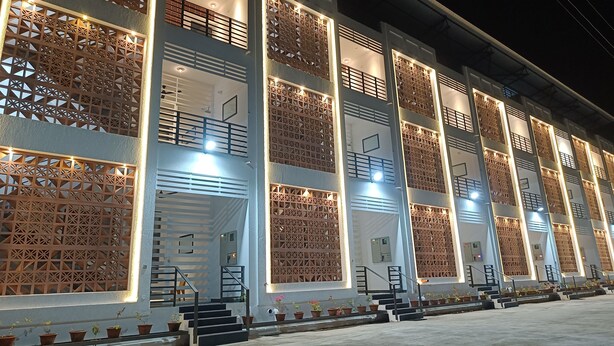 A multi-story building with a modern architectural design, featuring balconies with intricate wooden latticework and illuminated entryways. - Devaki Resort (Puducherry)