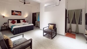 A modern hotel room with a bed, two ceiling fans, an air conditioning unit, a chair, a small table, and a painting on the wall. - Devaki Resort (Puducherry)