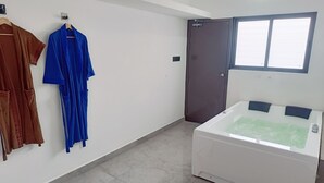 A bathroom with a bathtub, a towel rack with robes, and a door. - Devaki Resort (Puducherry)