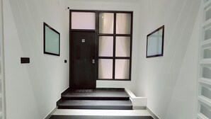 A hallway with a dark door, a small step leading to a landing, and a black mat at the entrance. - Devaki Resort (Puducherry)