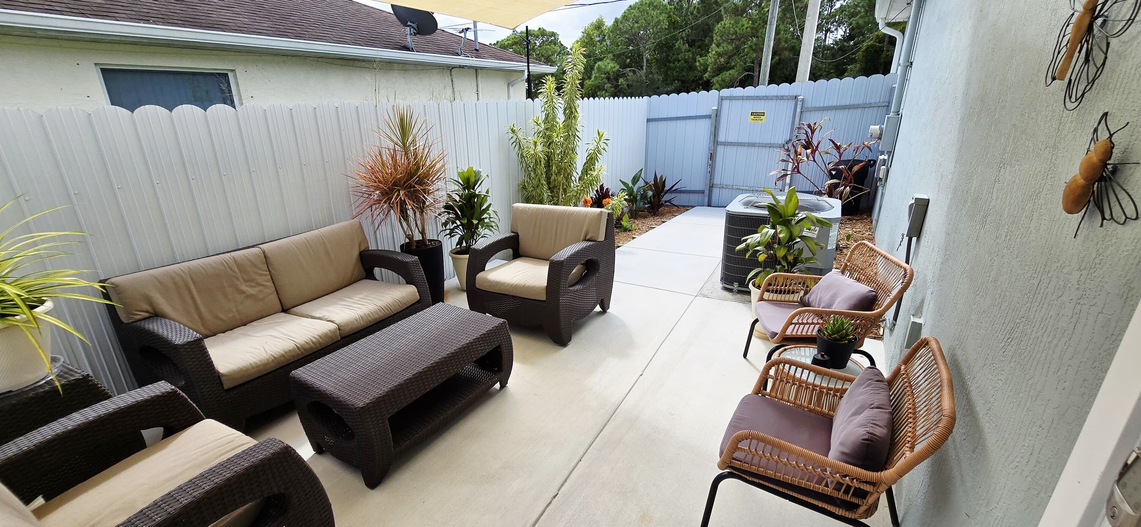 Une terrasse aménagée dans le jardin, avec un canapé, des chaises et une table, le tout entouré de plantes en pot.