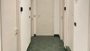 A narrow hallway with white walls and green-tiled flooring, leading to a closed door at the end. - Big fish Affittacamere (Alghero)