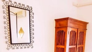 A room with a dining table set for two, a wooden cabinet, and a decorative mirror on the wall. - Big fish Affittacamere (Alghero)