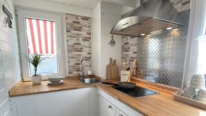 A compact kitchen with white cabinets, a wooden countertop, a stainless steel sink, and a modern ventilation hood. - Tiny Haus am Meer (Heringsdorf)