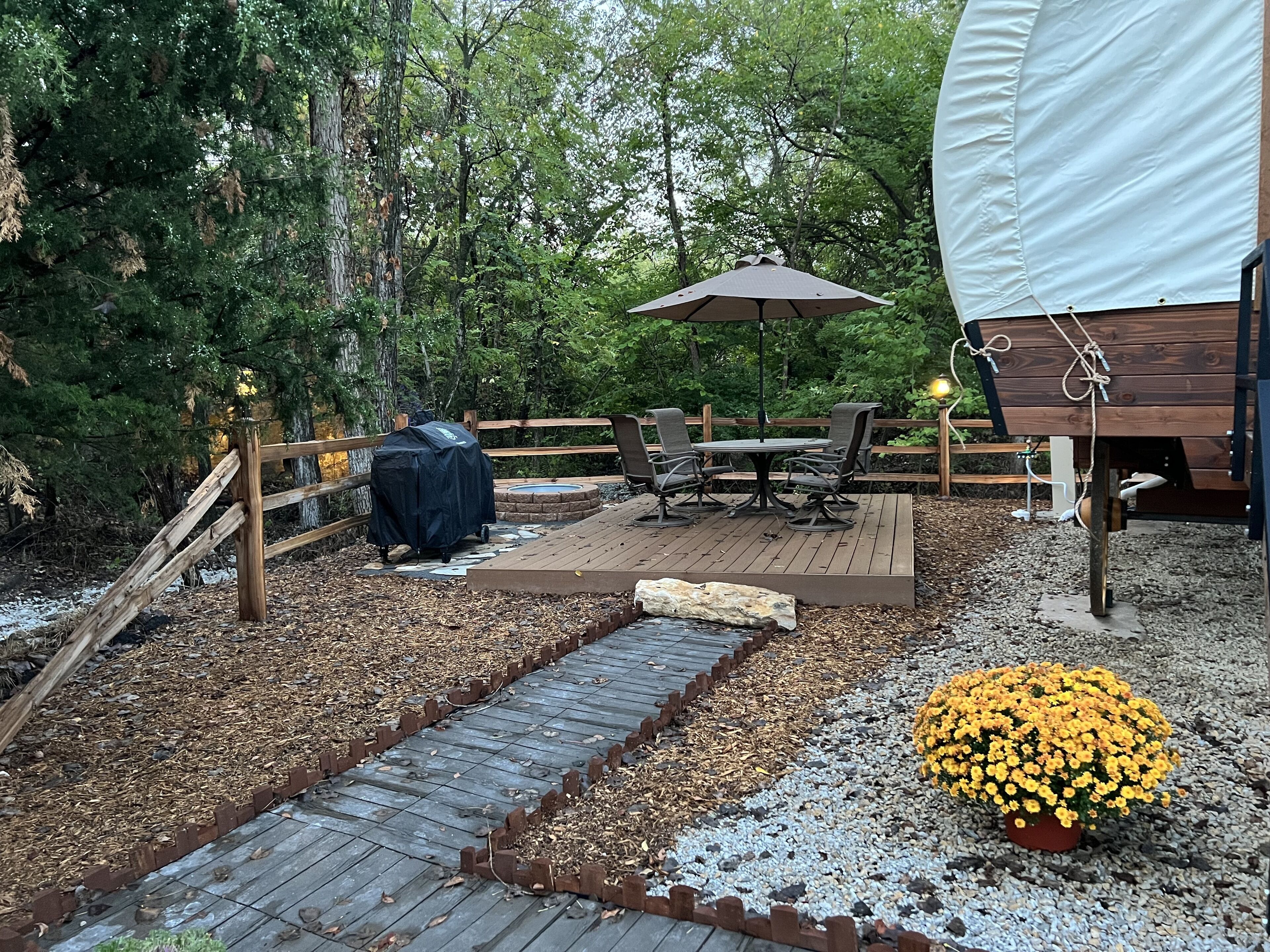 En träaltan med ett bord och stolar, omgiven av ett trästaket och en överbyggd grillplats.