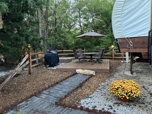 Une terrasse en bois avec une table et des chaises, entourée d’une clôture en bois et agrémentée d’un barbecue couvert.