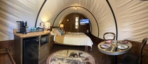 Un hébergement confortable en forme de tente, comprenant un lit, un petit bureau avec une machine à café, une table ronde avec des assiettes et un tapis à motifs animaliers.