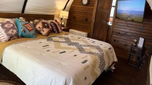 Una habitación acogedora con cama, almohadas, un reloj, un televisor y una pared de madera.