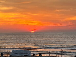 A sunset over the ocean with a pier and people in the foreground.