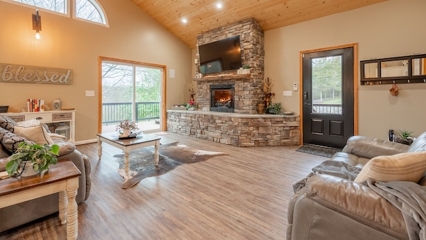 A spacious living room with a stone fireplace, leather sofas, and a large window. - Secluded 5 BR Modern Cabin, 120 acres. New River Trail, Claytor Lake, VA tech (Draper)