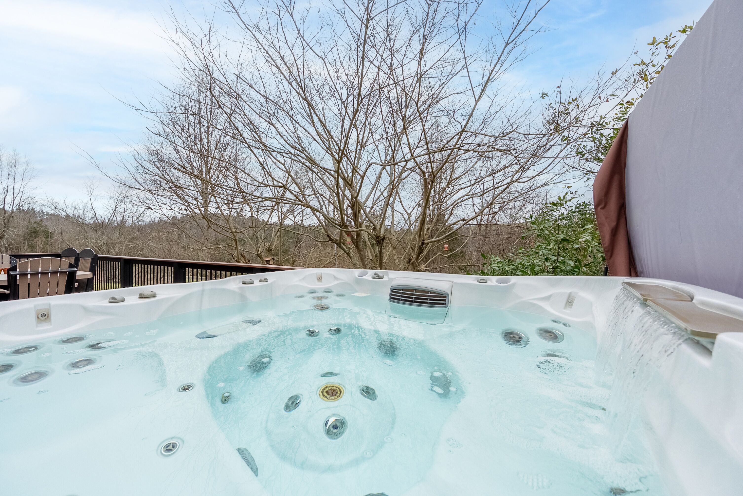 A hot tub with a clear view of the surrounding area, including a wooden deck and leafless trees.