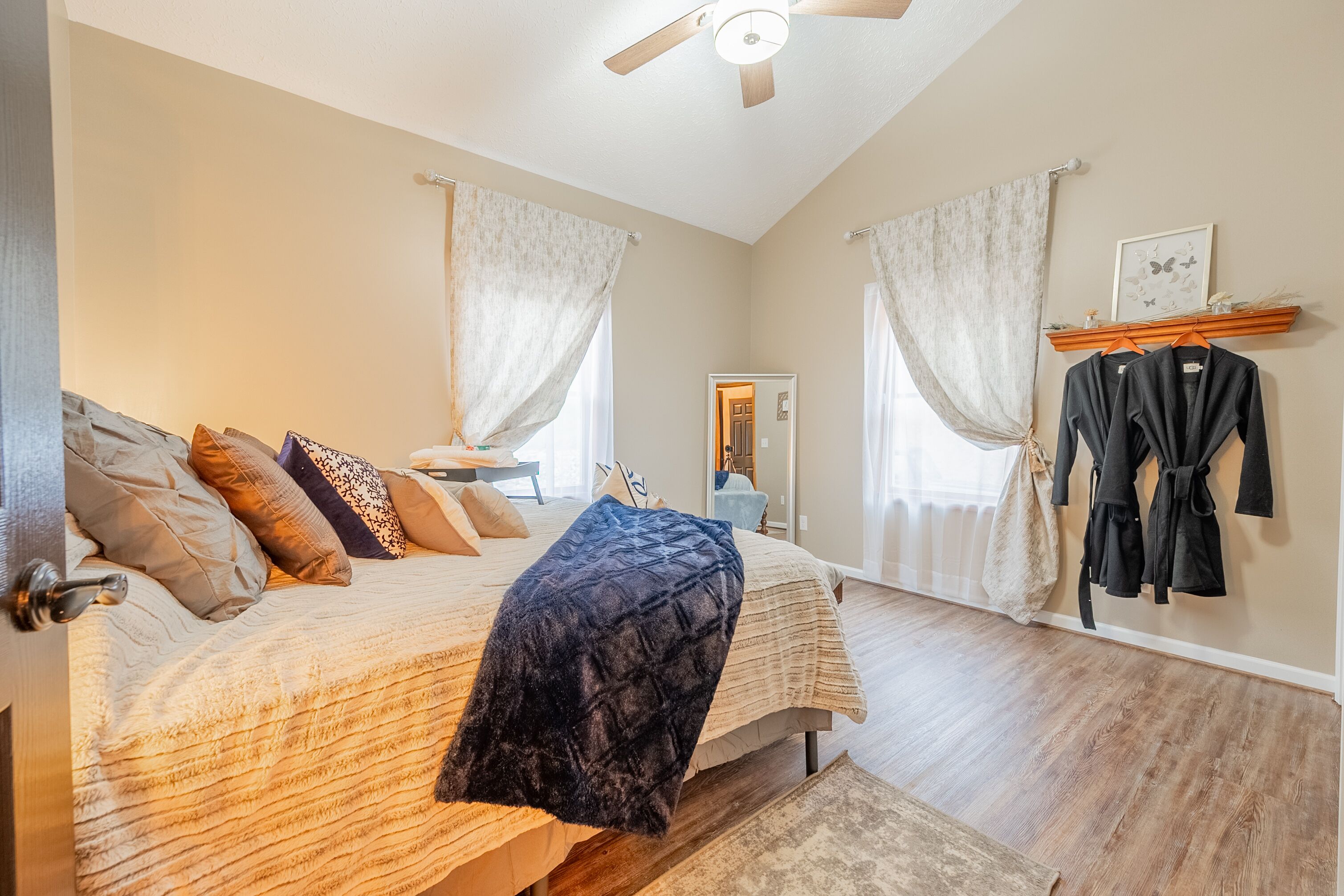A bedroom with a bed, a ceiling fan, a wooden floor, and a window with curtains.