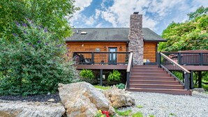 A log cabin with a stone chimney, a wooden deck, and a gravel driveway. - Secluded 5 BR Modern Cabin, 120 acres. New River Trail, Claytor Lake, VA tech (Draper)