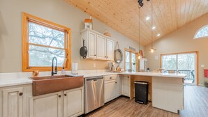A modern kitchen with wooden cabinets, a stainless steel dishwasher, and a large island with a sink. - Secluded 5 BR Modern Cabin, 120 acres. New River Trail, Claytor Lake, VA tech (Draper)