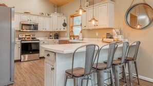 A modern kitchen with white cabinetry, stainless steel appliances, and a central island with bar stools. - Secluded 5 BR Modern Cabin, 120 acres. New River Trail, Claytor Lake, VA tech (Draper)
