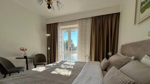 Habitación de hotel con una cama grande, un escritorio y una silla. Se ve una ventana con cortinas, y un candelabro.