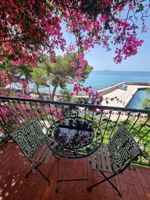 Un balcon avec une table et des chaises en métal, donnant sur une piscine et la mer.