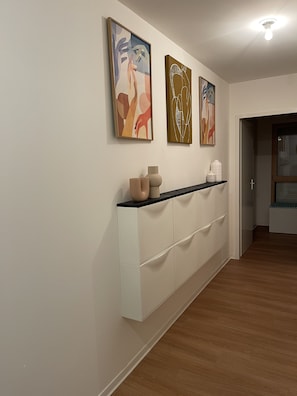 A hallway with a white cabinet, three abstract paintings, and a ceiling light. - Cosy Maia (Nantes)