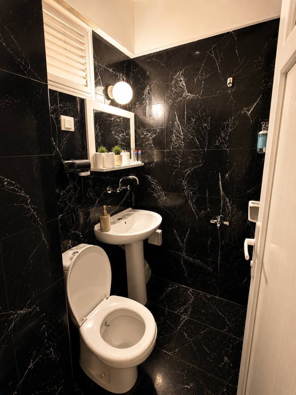 Un bagno con il water, un lavandino, uno specchio e pareti in marmo nero.