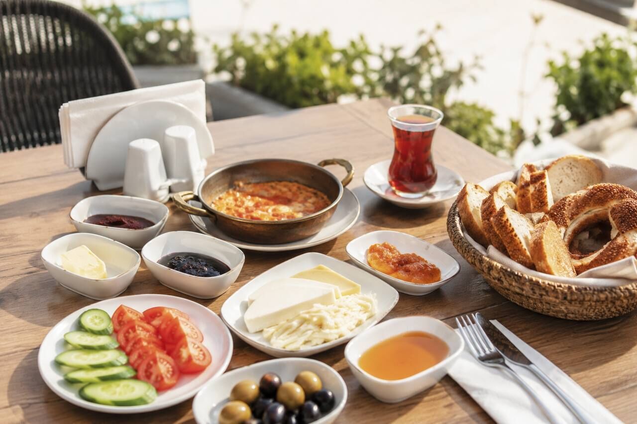 Ein Tisch mit verschiedenen Speisen, darunter Brot, Käse, Oliven, Tomaten und eine Tasse Tee.