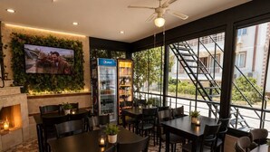 A restaurant with stone-tiled flooring, black tables and chairs, a ceiling fan, a television mounted on a wall, and a Pepsi refrigerator. - Brand otel (Didim)