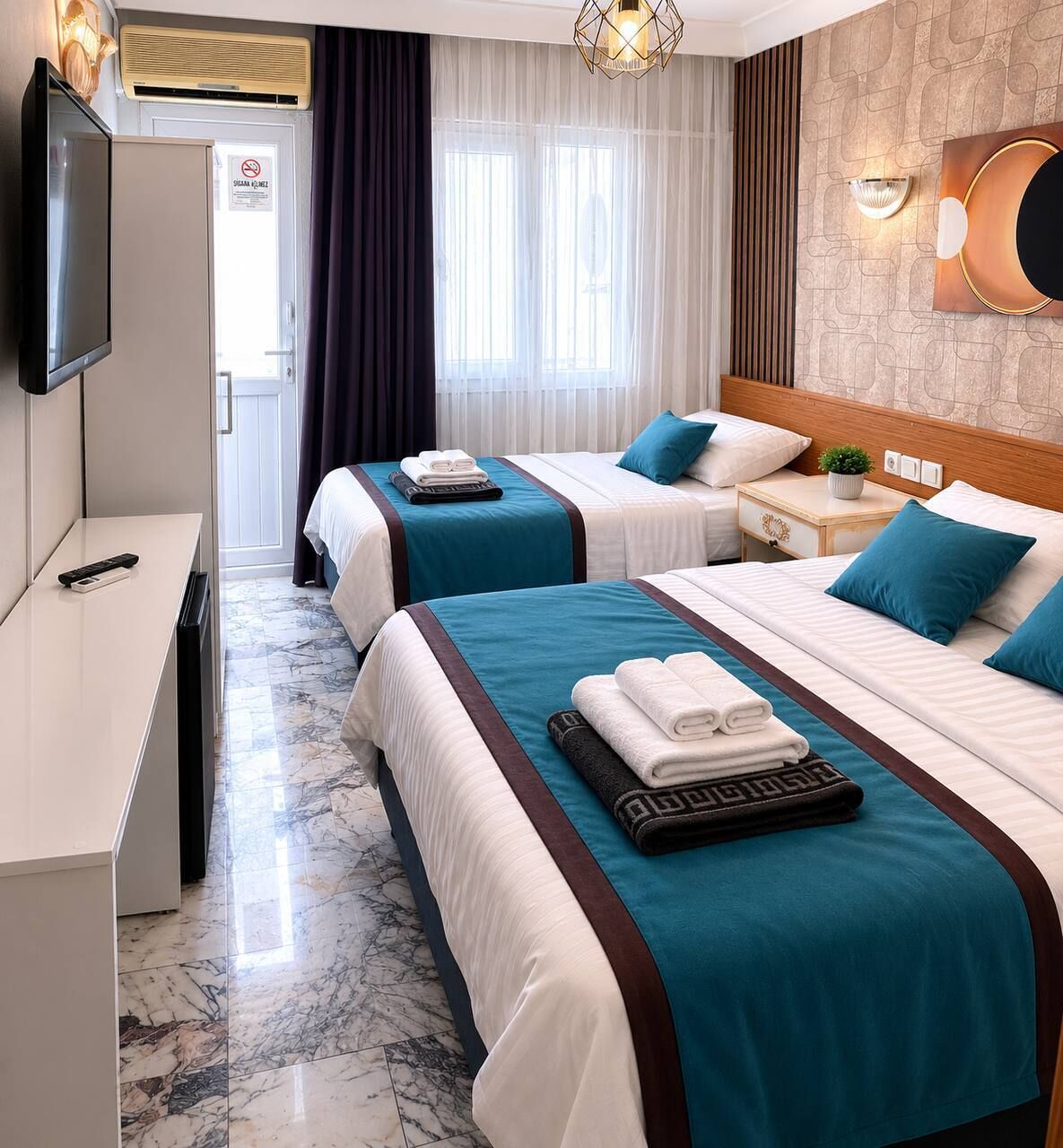 A hotel room with two beds, a TV, a desk, a nightstand, and a wall-mounted light fixture.