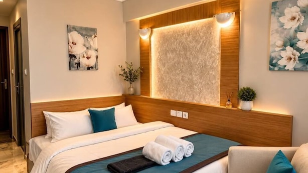 A modern hotel room with a large bed, a seating area, a wooden headboard, a wall-mounted light, and a ceiling light fixture. - Brand otel (Didim)