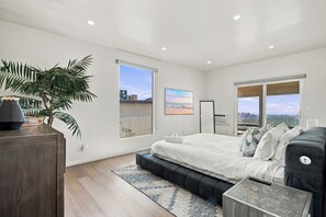 Ein modernes Schlafzimmer mit einem großen Bett, Blick auf die Stadt und einer Zimmerpflanze.