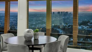 Un espace repas avec vue sur la ville, de grandes fenêtres et une table ronde entourée de chaises.