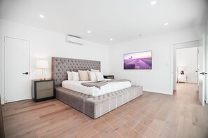 Une chambre moderne avec une tête de lit capitonnée, un grand lit, une table de chevet avec une lampe et un tableau encadré au mur.