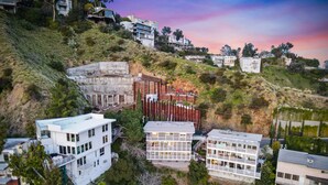 Un quartier résidentiel situé sur une colline, avec des maisons modernes, notamment une maison blanche à deux étages dotée d’un balcon et une grande maison blanche avec un toit plat.