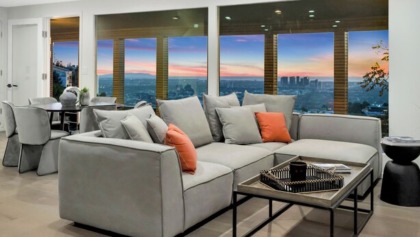 Un salon moderne avec un canapé gris, une table basse et une vue sur la ville, visible à travers de grandes fenêtres.