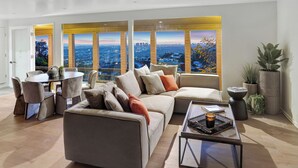Un salon moderne doté d’un grand canapé d’angle, d’une table à manger et d’une table basse. De grandes fenêtres offrent une vue sur la ville.