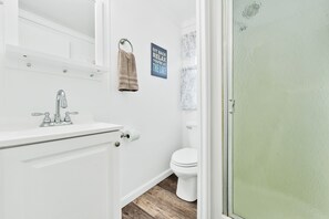 Et badeværelse med en hvid vask, toilet og en brustdør.