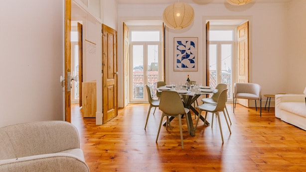 A spacious dining area with a wooden floor, a round table set for six, and a large window offering a view of the city. - RENT4REST CASTLE VIEW FAMILY & FRIENDS BAIRRO ALTO (Lisboa ciudad)