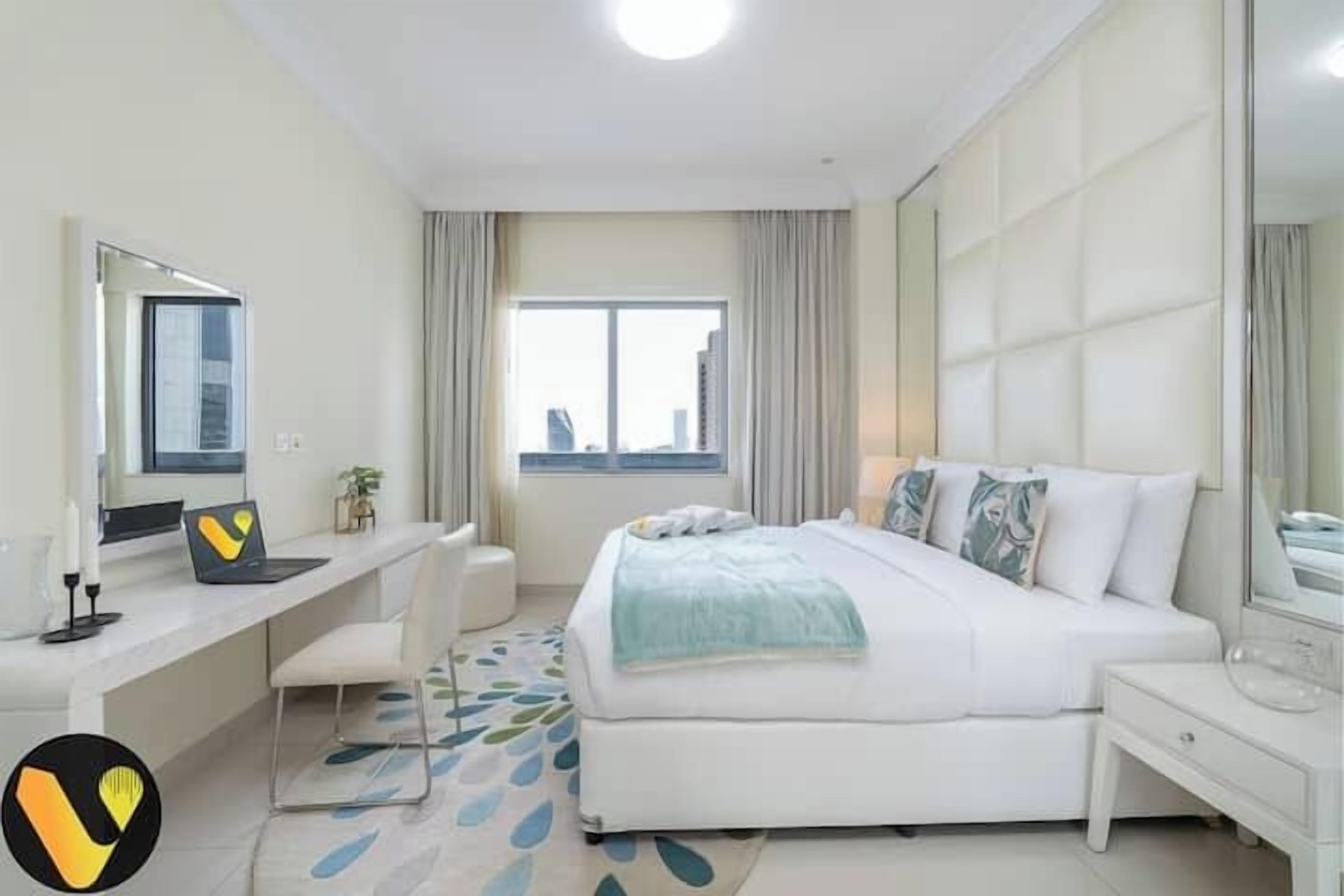 A modern hotel room with a large bed, a desk with a laptop, a chair, and a window with curtains.