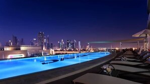 Ein Poolbereich mit Liegestühlen und Blick auf die nächtliche Skyline der Stadt.