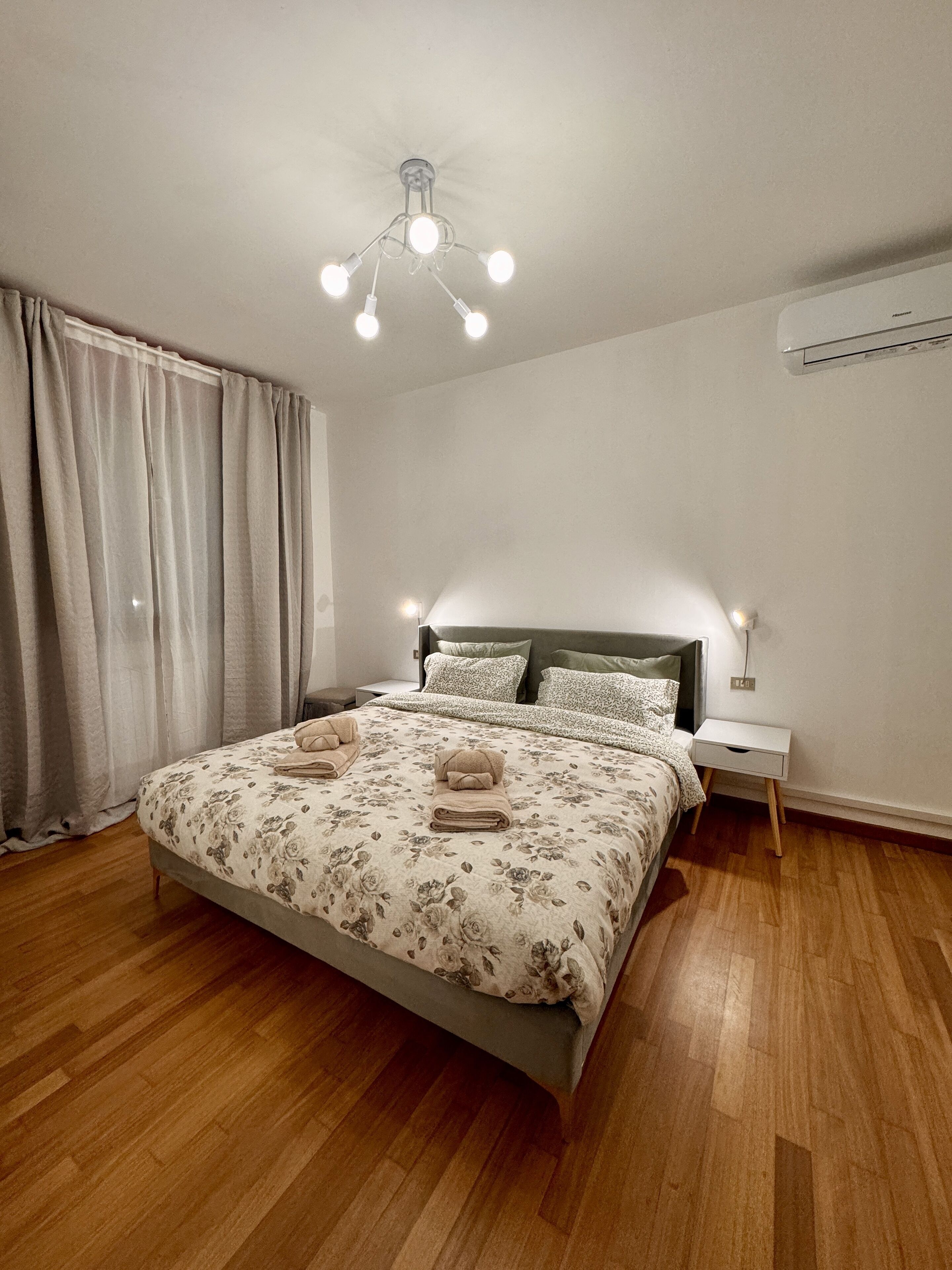 Een slaapkamer met een bed, een nachtkastje, een lamp en een plafondarmatuur.