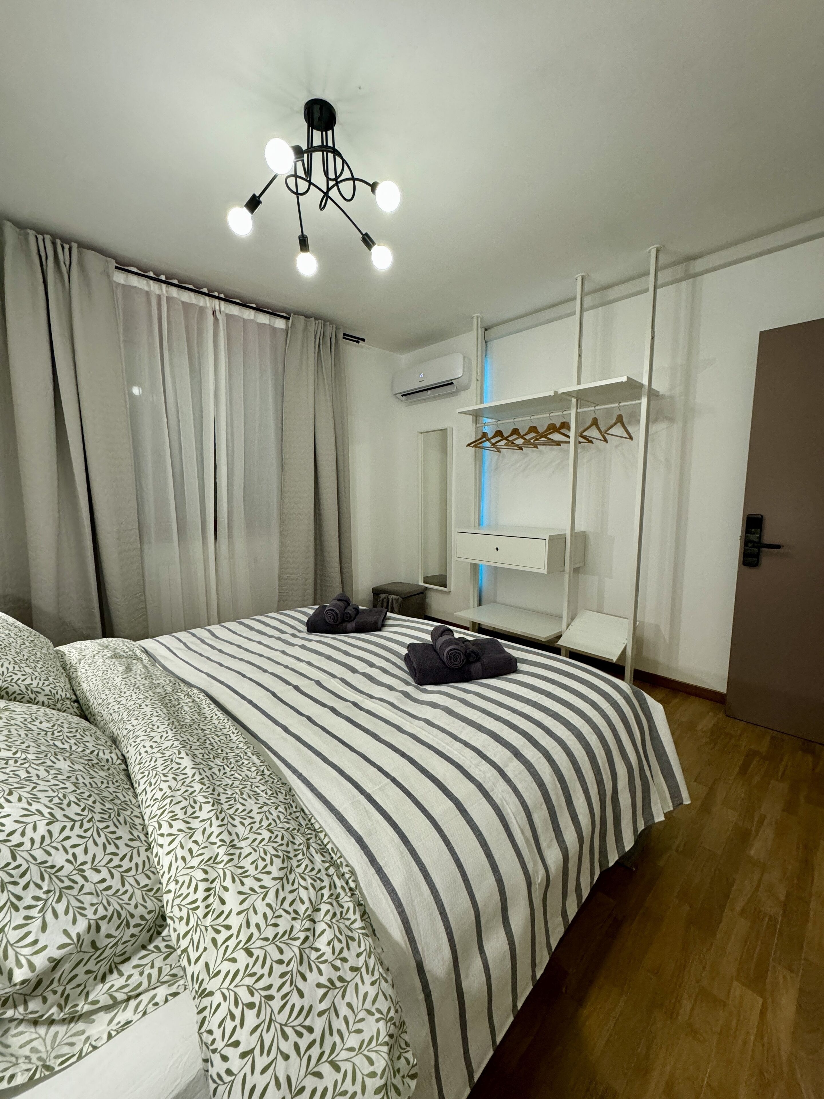 Ein modernes Hotelzimmer mit einem großen Bett, einer Deckenleuchte, einem Kleiderschrank und einem Spiegel.