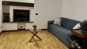 Een woonkamer met een houten vloer, een glazen salontafel, een donkerblauwe bank en een klein houten bijzettafeltje met een plant.