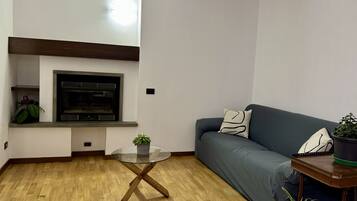 Ein Wohnzimmer mit Holzboden, einem Glastisch, einem dunkelblauen Sofa und einem kleinen Holztischchen mit einer Pflanze.