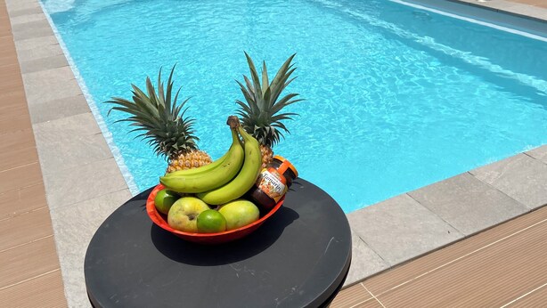 A swimming pool with a tropical fruit bowl on a table in the foreground.