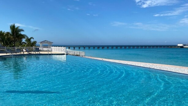 Ein klares, blaues Schwimmbecken mit Liegestühlen, eine Pier, die ins Wasser ragt, und ein klarer Himmel.