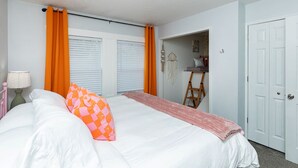 Un dormitori amb un llit, cortines taronges, una escala i una porta blanca.