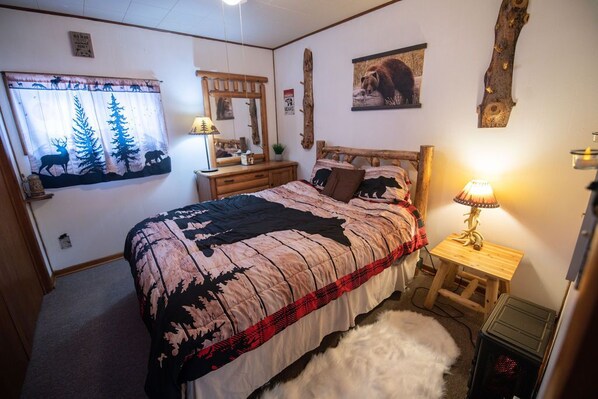 A bedroom with a bed, a nightstand, a lamp, a mirror, and a wall with a bear picture.