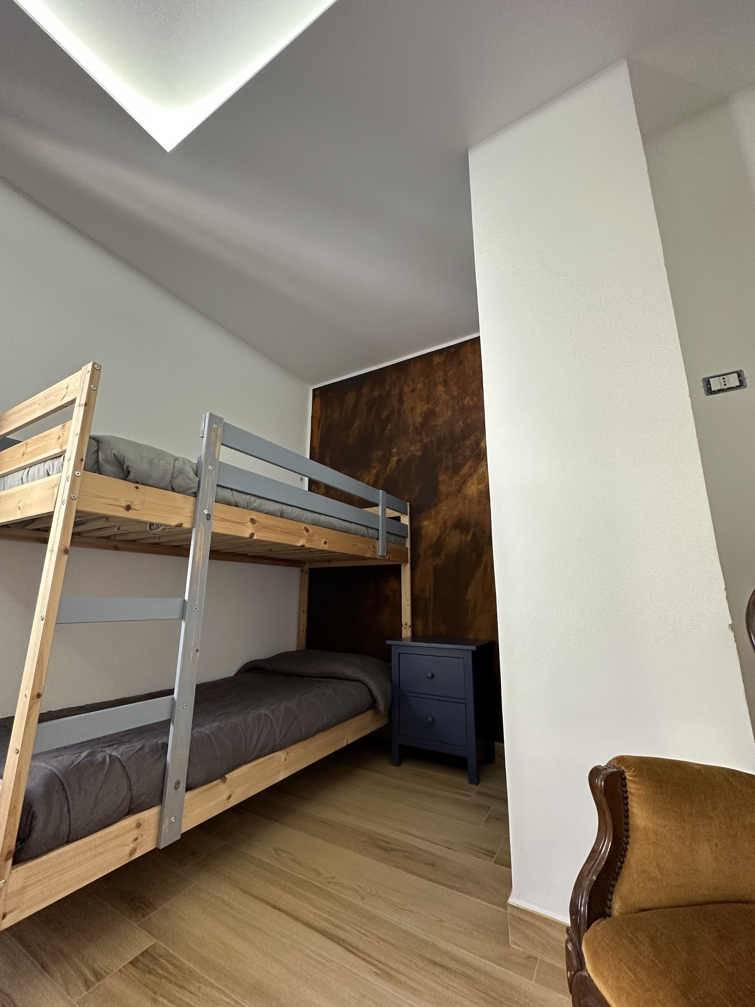 Une chambre avec un lit superposé, un plancher en bois, une table de chevet et une chaise.